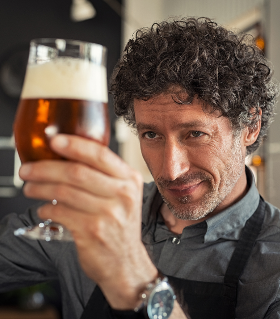 Man looking at a glass of beer intently that he's holding in the air