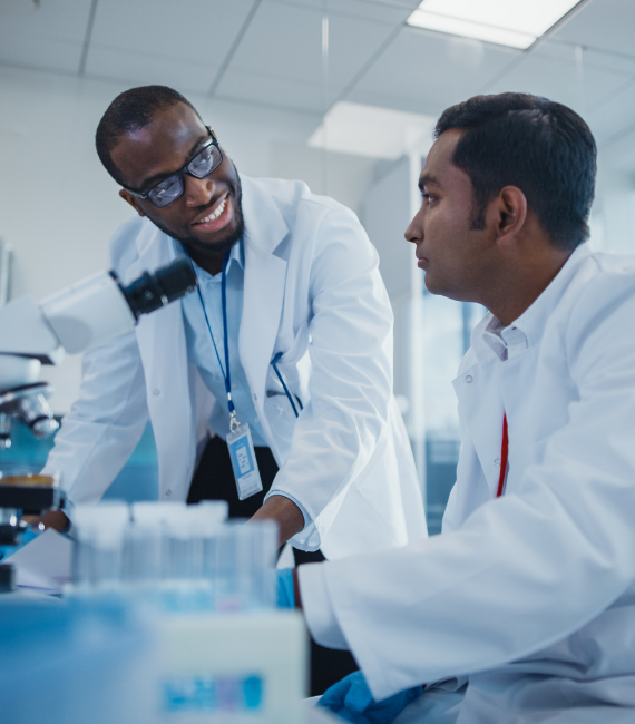 Two men in a lab near a microscope talking