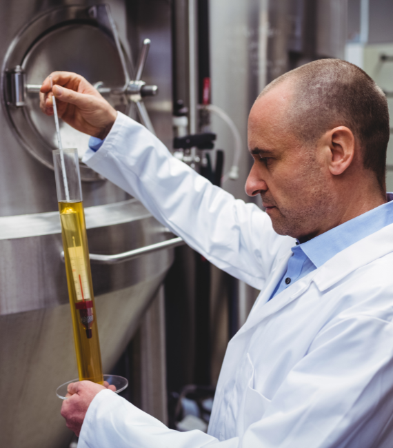 Man standing in front of large production equipment sampling a liquid with respective testing tool